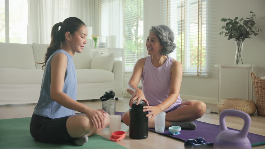 Young adult child active mature middle age old mum drink whey protein shake bottle diet food after home workout. Love health care older aged mom asia elder people happy relax sport protect aging life.