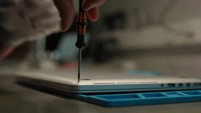 Technician wearing gloves using screwdriver to disassemble laptop computer on workbench, performing maintenance and repair tasks, close-up. Concept of computer hardware, repairing, upgrade, technology - Powered by Shutterstock - Get 15% off with code: PIKWIZARD15