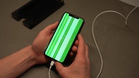 Technician plugging charging cable into broken smartphone showing green screen with glitches, indicating potential hardware or software issues requiring repair or troubleshooting, slow motion, closeup - Powered by Shutterstock - Get 15% off with code: PIKWIZARD15