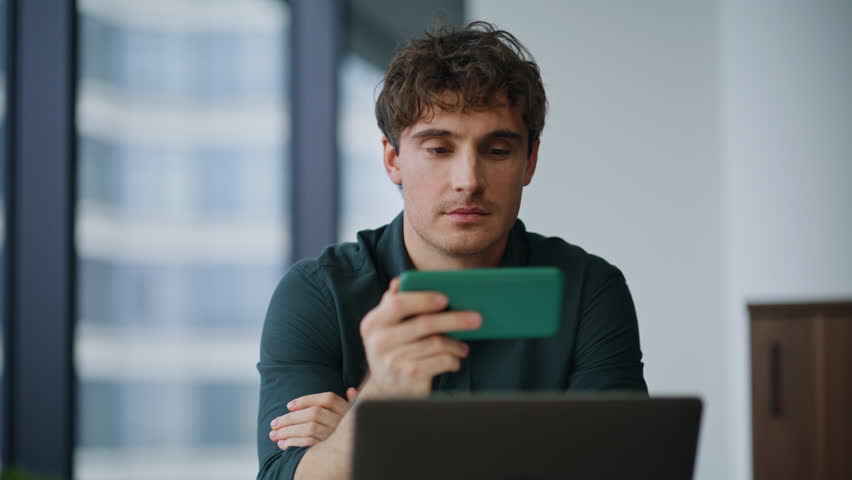 Employee watching cellphone video at company workplace closeup. Relaxed manager browsing social media content holding horizontal smartphone. Smiling corporate worker shopping online taking break.