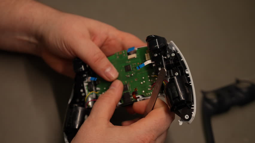 Technician hands inspecting disassembled video game controller, revealing intricate joystick mechanics and detailed electronic circuitry. Concept of professional electronics repair and maintenance.