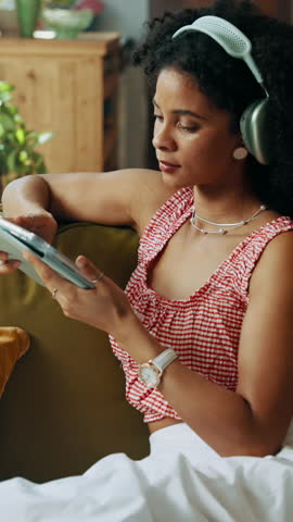 Headphones, tablet and woman on sofa in home on app for listening to music, podcast or radio. Digital technology, relaxing and female person streaming album, playlist or song in living room.