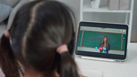 Rear view of young student learning online class with teacher at home. Adorable child student wearing headphones, using digital tablet study from school tutor by virtual remote online in living room. - Powered by Shutterstock - Get 15% off with code: PIKWIZARD15
