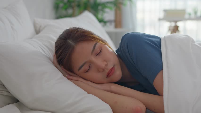 Asian beautiful woman lying down on bed in bedroom in morning at home. Attractive young girl feel happy and relax, sleeping with cozy pillow and blanket enjoy early day in holiday weekend in house.