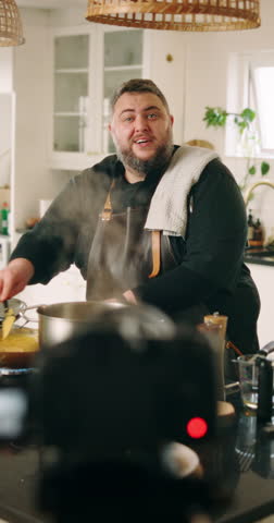 Cooking, live streaming and man in kitchen with food for culinary lesson, meal tutorial and dinner in home. Camera, influencer and chef with ingredients for nutrition, gourmet recipe and cuisine