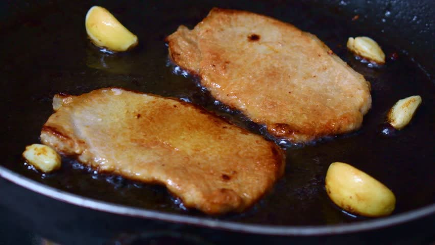 Pan fried pork chop with garlic in a pan.	