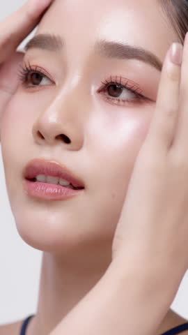 Vertical footage beautiful young Asian woman with healthy facial skin isolated over white background for skincare commercial product advertising. Slow motion shot.