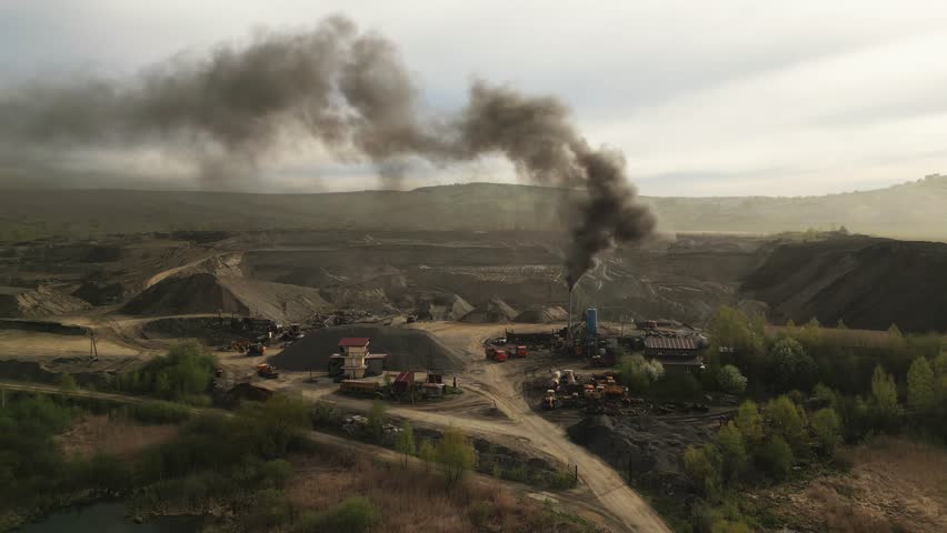 Smoke rises from machinery at an industrial mining site located in a remote area. The early morning light casts shadows on the rugged landscape surrounding the operations.