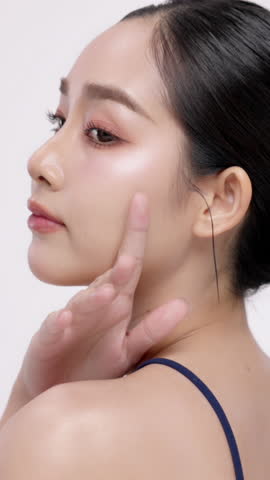 Vertical footage beautiful young Asian woman with healthy facial skin isolated over white background for skincare commercial product advertising. Slow motion shot.