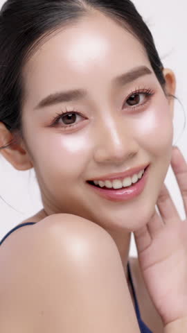 Vertical footage beautiful young Asian woman with healthy facial skin isolated over white background for skincare commercial product advertising. Slow motion shot.