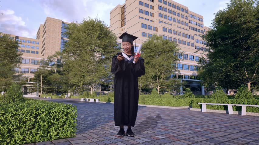 Full Body Of Asian Woman Student Graduates In Cap And Gown With Diploma Looking At Smartphone Then Saying Wow In Front Of A Magnificent University Building