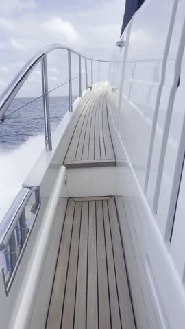 Handheld Walk Along Luxury Motor Yacht Side Deck Toward Foredeck While Cruising at Full Speed on Calm Sea with Dramatic Storm Clouds on Horizon, Showing Panoramic View of Upper Deck and Dark Gray Sky