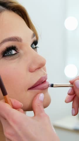 close up Professional lips Makeup, beautician applies lipstick, Beautiful woman face, Hand of make-up master in beauty salon, painting lips, Make up in process 