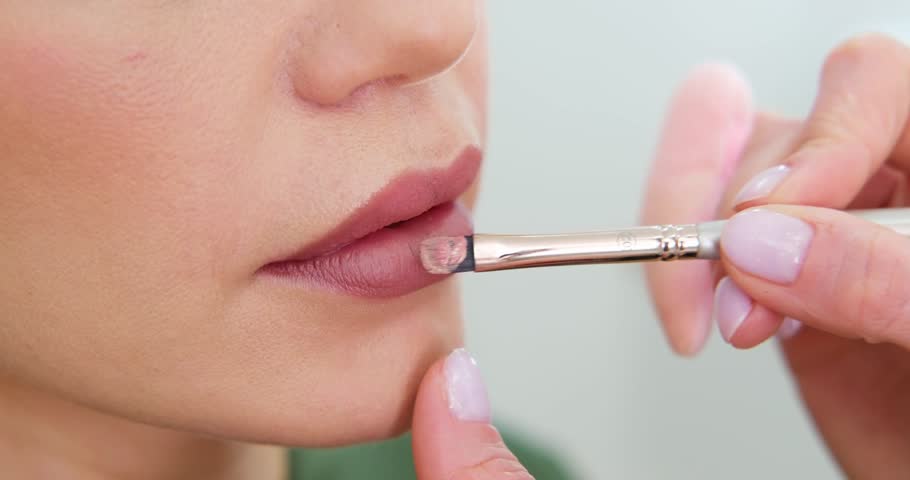 close up Professional lips Makeup, beautician applies lipstick, Beautiful woman face, Hand of make-up master in beauty salon, painting lips, Make up in process 