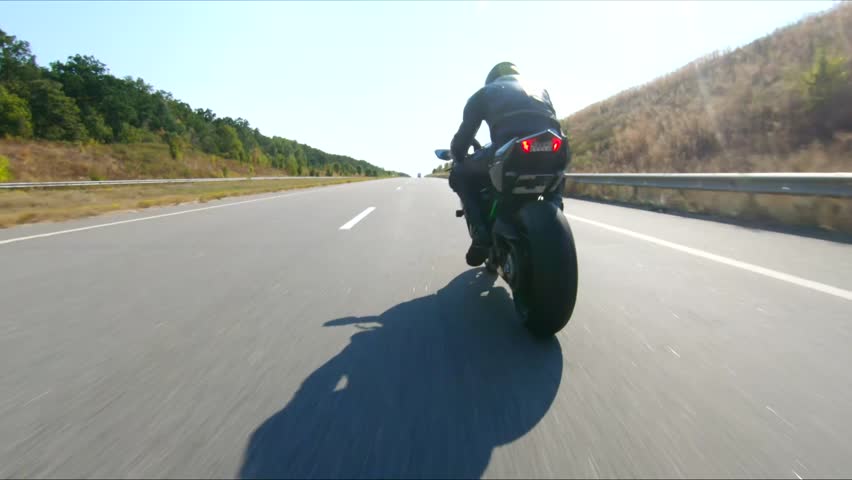 Biker is driving motorbike during road trip at summer day. Man ride fast on modern sport motorcycle at highway. Motorcyclist racing his bike on country road. Concept of adventure. Aerial shot