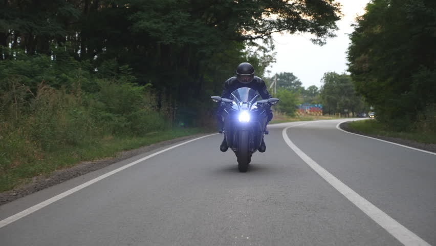 Man riding on modern sport motorbike at rural road near forest. Motorcyclist racing his motorcycle on country route. Guy driving bike during trip. Concept of freedom lifestyle and adventures. Slow mo