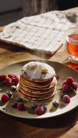 Sprinkling sugar powder on stack of delicious pancakes. Close-up shot beautiful arrangement of berries and powdered sugar on plate. Treat for eyes and taste buds. Vertical video. Gluten free food