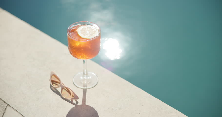 Swimming pool, glass and cocktail with sunglasses for holiday, summer vacation or relax outdoor. Water, alcohol and drink at hotel resort for tourism, travel and luxury with fresh lemon in top view