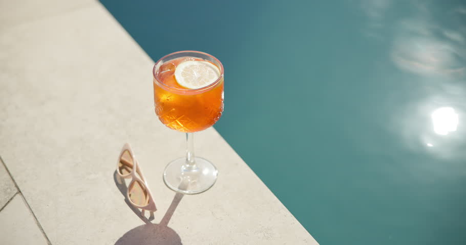 Swimming pool, glass and cocktail with sunglasses for holiday, summer vacation or relax outdoor. Water, alcohol and drink at hotel resort for tourism, travel and luxury with fresh lemon in top view