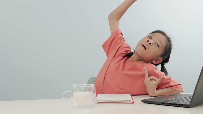 Cute Asian elementary school age kid girl yawning while studying online in class with friends and drinking glass of milk to refresh herself. Homeschooling concept. isolated white background.