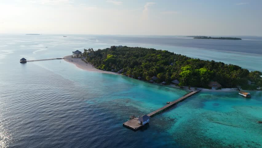Aerial view zoom in of tropical Maldives island with wooden pier surrounded by turquoise sea, bright daylight and lush greenery, summer escape, travel agency, hotel resort