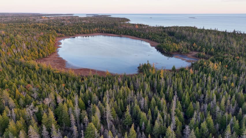 Aerial drone shot of a circular forest lake in Michigan’s Upper Peninsula during fall, surrounded by vibrant trees