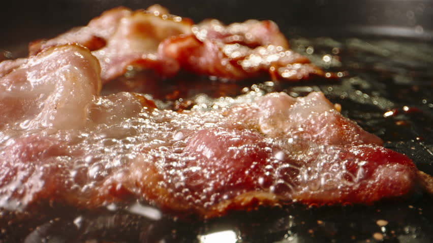 Frying pork bacon in pan side view macro shot slow motion. Gorgeous perfect appetizing fried slice of bacon in boiling fat in frying pan. Fried to perfect. Juicy bacon flavorful and satisfying. Fat