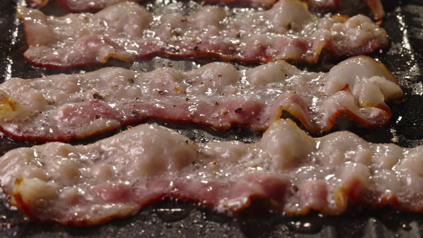 Frying halal beef bacon in pan side view close up. Pan-fried bacon slices capture the essence of sizzling goodness, ready to be devoured with delight. Juicy halal beef bacon flavorful and satisfying