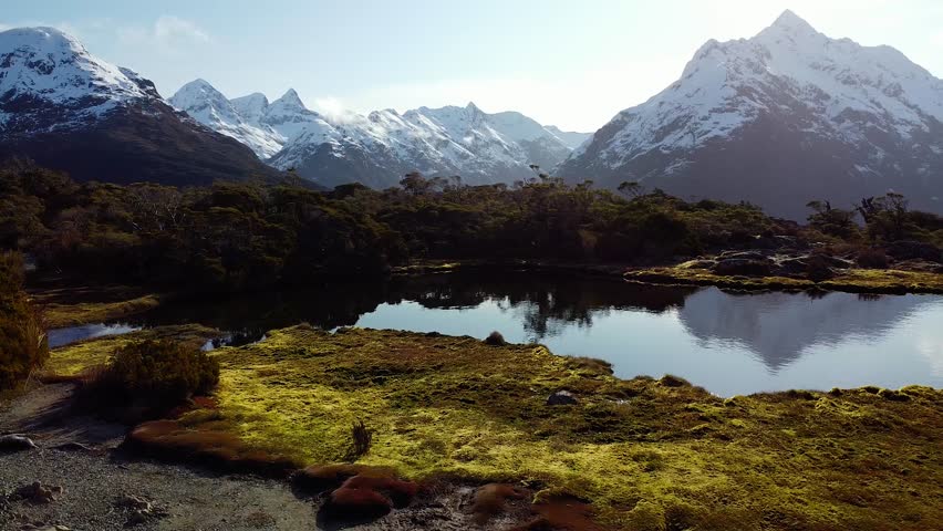 Aerial flyover Beautiful landscape with lake and sun reflection in New Zealand. Snowy mountains and sunrise in background. Key Summit in Fiordland National Park, New Zealand.