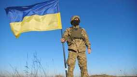 Ukrainian army man in military uniform lifting national banner. Young male soldier holds a waving flag of Ukraine against blue sky. Victory against russian aggression. Invasion resistance. Low view - Powered by Shutterstock - Get 15% off with code: PIKWIZARD15