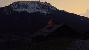 Swiss flag waving gently on a traditional chalet roof with a majestic snowy mountain in the background during a peaceful sunset - Powered by Shutterstock - Get 15% off with code: PIKWIZARD15