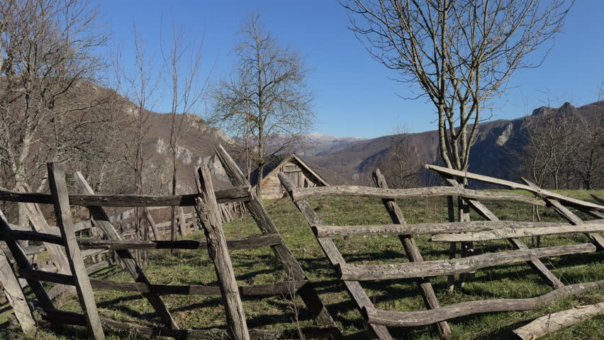 dolly shot of old wooden fence that fell down in front of old wooden house in a village located on the top of a mountain with beautiful view. sunny clear day.