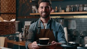 Smiling cheerful Caucasian male small business owner man cafe barista in uniform holding cappuccino cup worker employer giving coffee to client guy serving order staff working in cafeteria catering - Powered by Shutterstock - Get 15% off with code: PIKWIZARD15