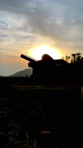 Traveler male uses mobile phone sitting in front of sunset.