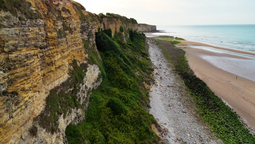 A flight along Omaha Beach’s coastline, showcasing green cliffs and the expansive sandy beach.