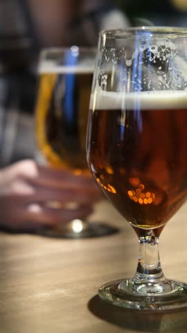 The concept of meeting friends in a bar. Close-up of two glasses of beer on a table, blurred background