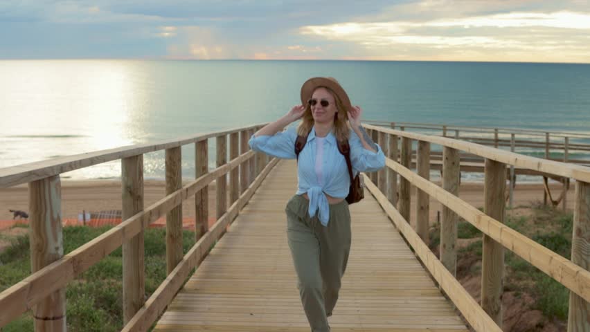 Female backpacker running on wooden pier, embodying travel freedom with adventurous spirit during golden sunset light.Travel, weekend, relax and lifestyle concept