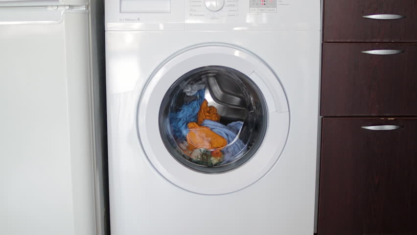 Laundry spinning inside modern washing machine drum, rotating wet clothes during cleaning cycle with continuous tumbling motion