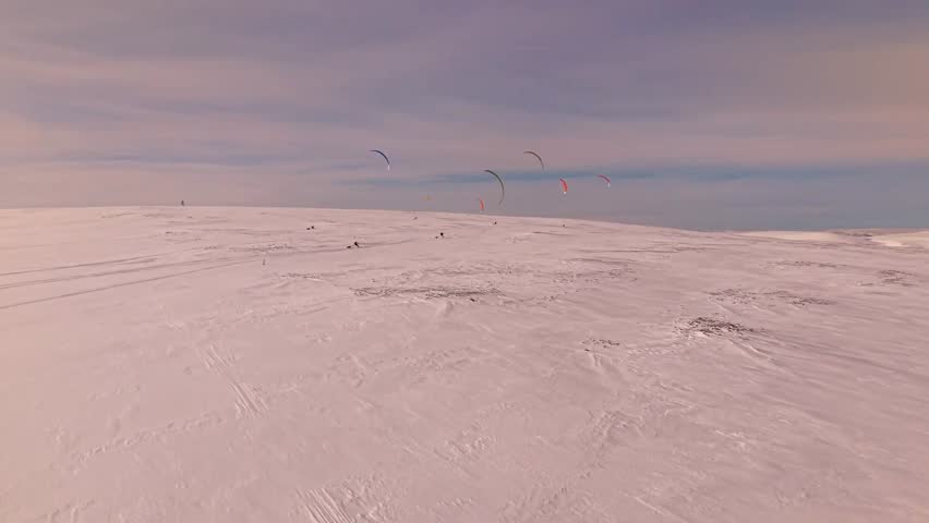 Gorgeous aerial drone footage of people flying and kite skiing with kites on vast large white snow covered Norway landscapes at an endurance race during a winter sunny day.