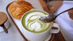 Skilled barista mixing intricate matcha latte art, creating delicate foam pattern inside ceramic cup, accompanied by golden croissant on minimalist surface - Powered by Shutterstock - Get 15% off with code: PIKWIZARD15