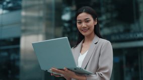 Portrait of young Thai woman holding laptop on city street looking at camera. Asian lady works on computer communicating with clients online. Female employee in urban environment - Powered by Shutterstock - Get 15% off with code: PIKWIZARD15
