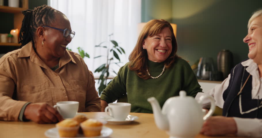 Embrace, happy and senior woman in lounge in home for communication. Tea, discussion and group hug of elderly friends in retirement talking, laughing bonding for relaxing in living room at house