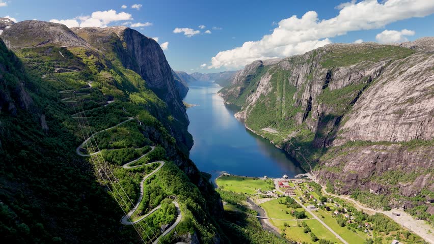 An aerial view of a winding road snaking through the lush green mountainsides, overlooking a serene fjord in Norway on a beautiful sunny day. Kjerag, Lysebotn, Lysefjorden, Norway