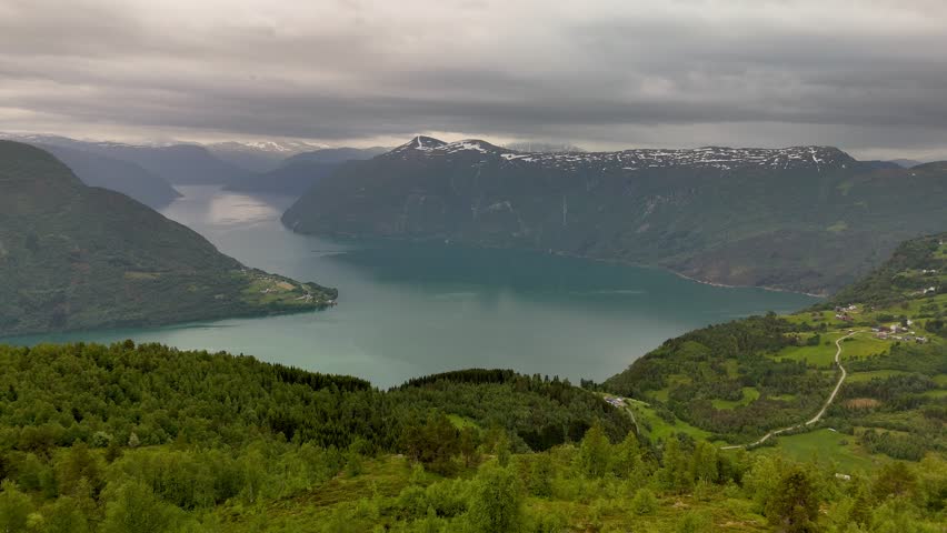 Nestled in the heart of Molden Norway, this breathtaking view captures a tranquil fjord surrounded by lush hills and snow-capped mountains. Misty clouds hover above, creating an enchanting atmosphere.