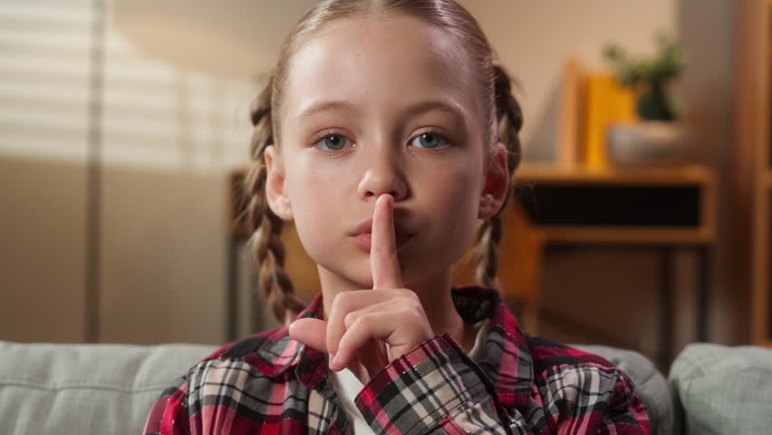 Close up portrait face headshot serious mystery child showing hush silent gesture silence forbidden speak secret information secrecy little Caucasian kid girl daughter baby at home looking at camera