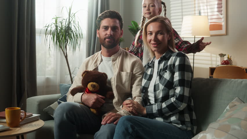 Portrait happy smiling healthy family at home looking at camera smile together at own apartment insurance bank medicine parents on couch with little daughter child kid baby girl hugging cuddling love
