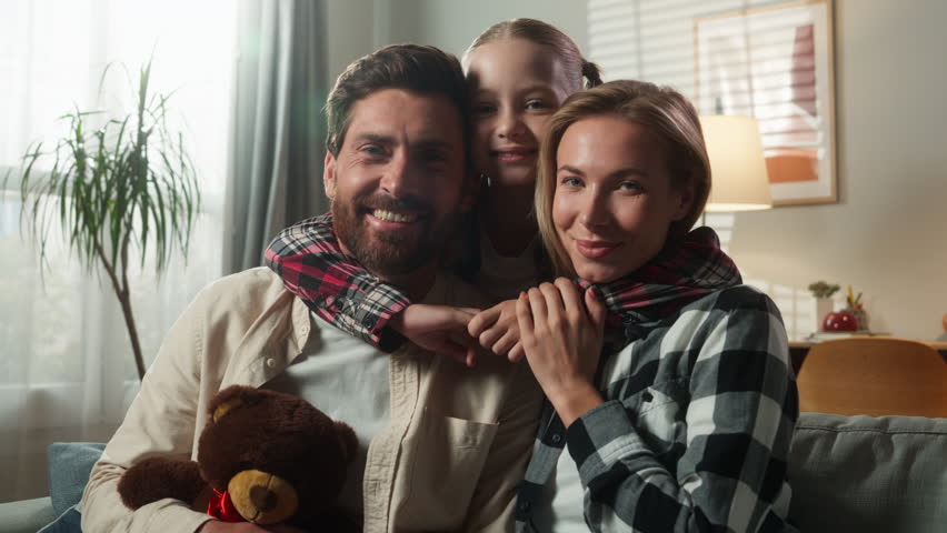 Portrait happy smiling healthy family at home looking at camera smile together at own apartment insurance bank medicine parents on couch with little daughter child kid baby girl hugging cuddling love