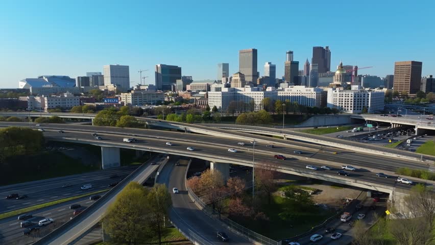 Atlanta , United States - 03 26 2025: Aerial backwards wide shot of traffic scene on elevated highway road in Atlanta, Georgia. Blue sky at golden sunset time in spring. Skyline with skyscrapers and t