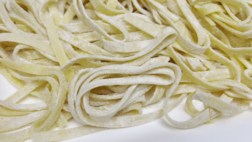 Mixture of wheat flour and egg yolk creating traditional Italian tagliatelle pasta, homemade noodles on board sprinkled with flour before cooking, healthy mediterranean cuisine
