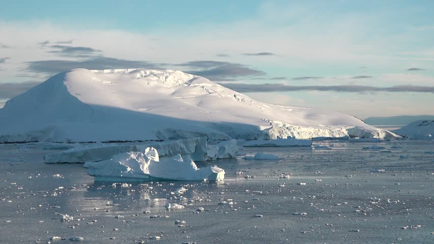 This breathtaking aerial perspective showcases a tranquil Arctic region filled with floating icebergs and majestic mountains. The clear blue sky enhances the scene